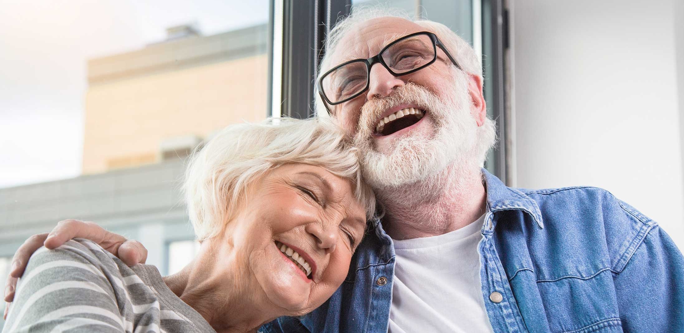 Ältere Frau und älterer Mann halten sich lachend im Arm.