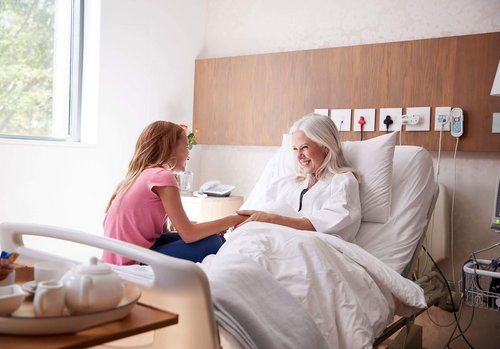 Alte Frau im Krankenbett hält die Hand eines jungen Mädchens, das auf dem Bett sitzt.